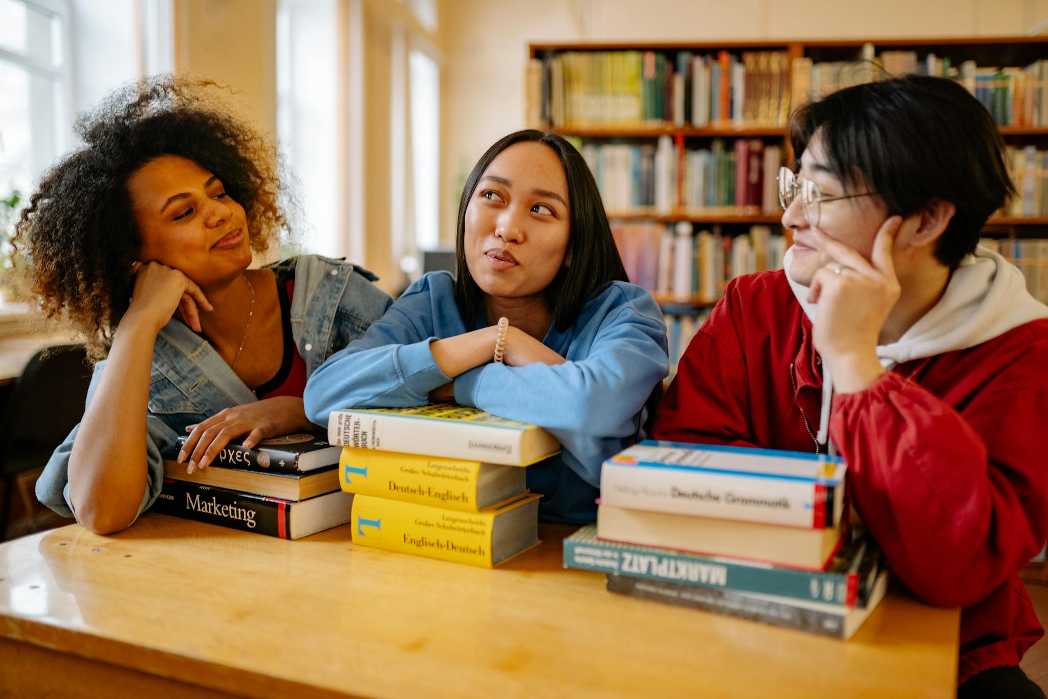 Three diverse students studying together in a university library with books around them.